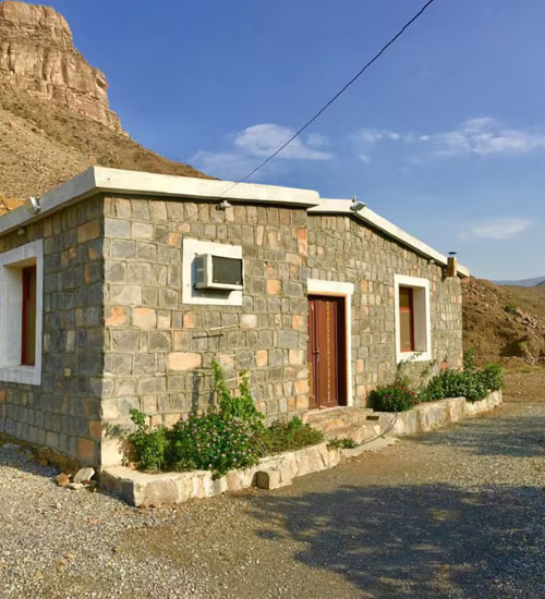 Stone-built Jebel Shams Villa with its garden and the mountain cliffs behind
